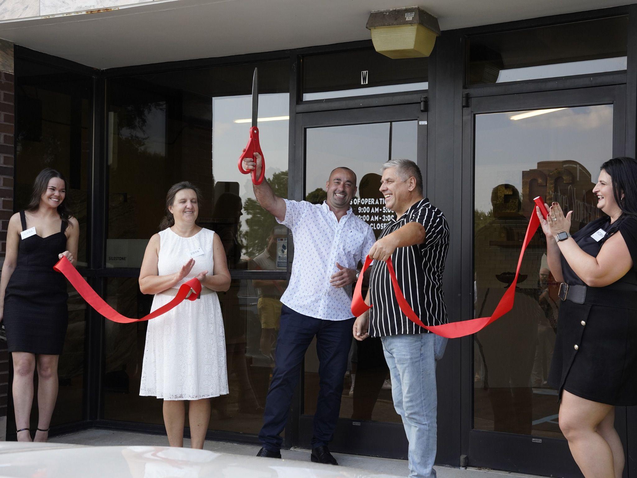 The founder, owner, and leadership team cut the ribbon to celebrate the Grand Opening of the new Clanton Road showroom. Large ceremonial scissors are held up in excitement, marking the official opening of East Coast Granite of Charlotte - Clanton Road. 